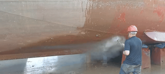 [Image placeholder]*Prompt: A close-up, detailed shot of a worker in full protective gear using an industrial sandblasting hose on the steel hull of a ship. Sparks and dust are visible as rust and old paint are stripped away, revealing the rough, clean metal underneath.*